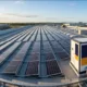 100kW-load-sizing-guide-hero - SunLith Energy SunLith Energy Rooftop solar panels stretch in long rows on a flat commercial roof under a clear sky. A large utility unit sits at the right side of the roof.
